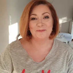 Portret kobiety z profesjonalnym makijażem, widoczne delikatne cieniowanie powiek i podkreślone kości policzkowe, włosy w odcieniach rudości.