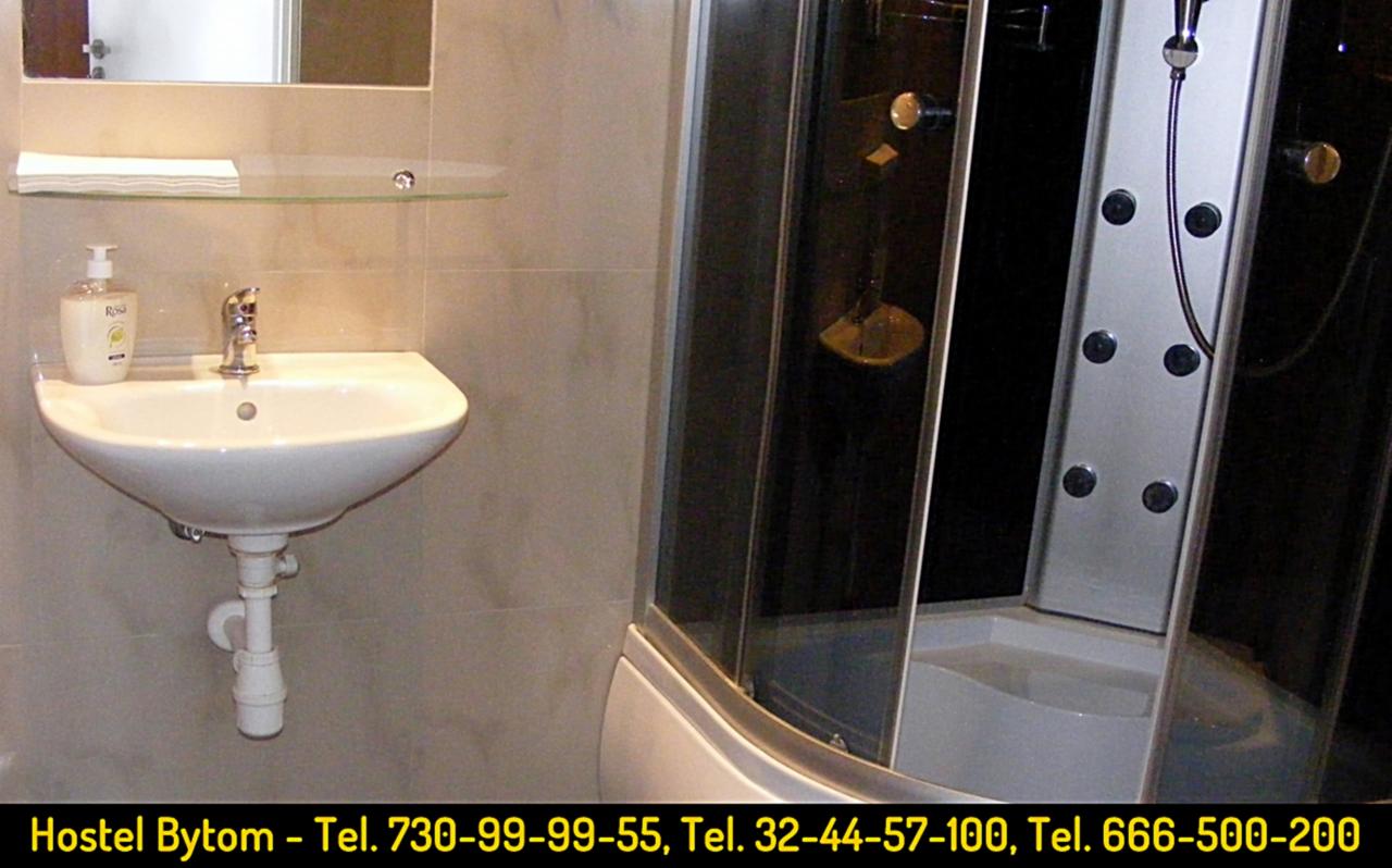 Łazienka w hostelu mPark Bytom: biała umywalka z mydłem w płynie, szklana półka nad nią, kabina prysznicowa z hydromasażem.