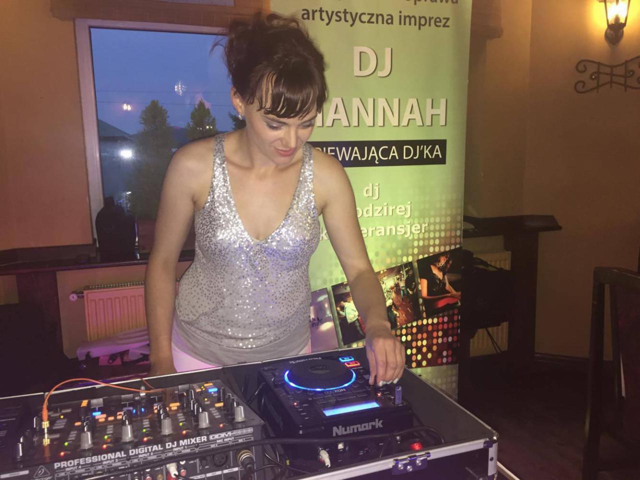 Kobieta DJ w srebrnym topie obsługuje mikser Numark na tle plakatu DJ Anny podczas imprezy.