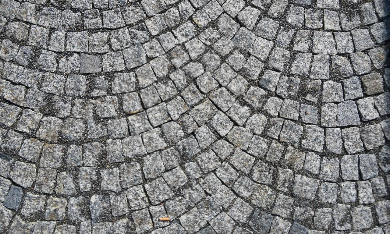 Ułożona z kostki granitowej nawierzchnia w kształcie wachlarza, widoczne drobne szczeliny wypełnione piaskiem, w dolnej części kadru niedopałek papierosa.