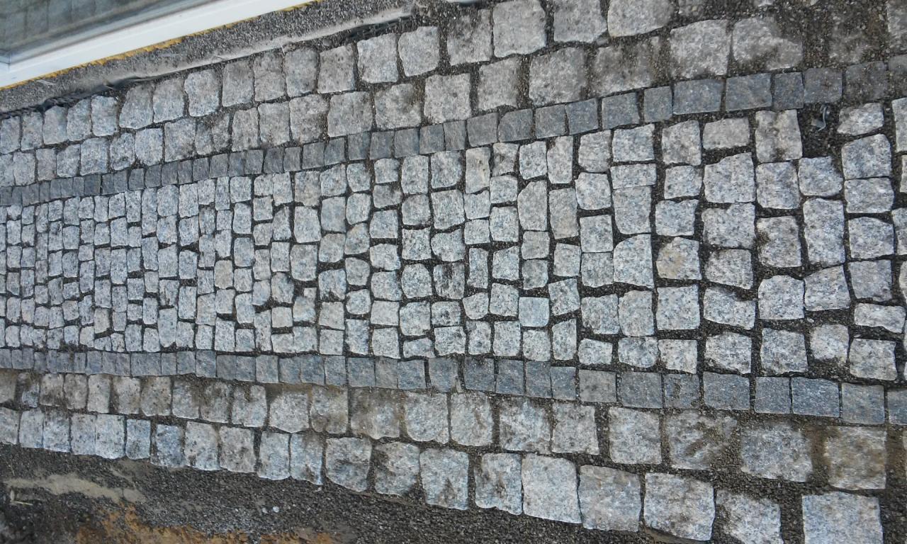 Ułożona z kostki granitowej szara nawierzchnia chodnika z ciemniejszymi obwódkami, widok z góry.