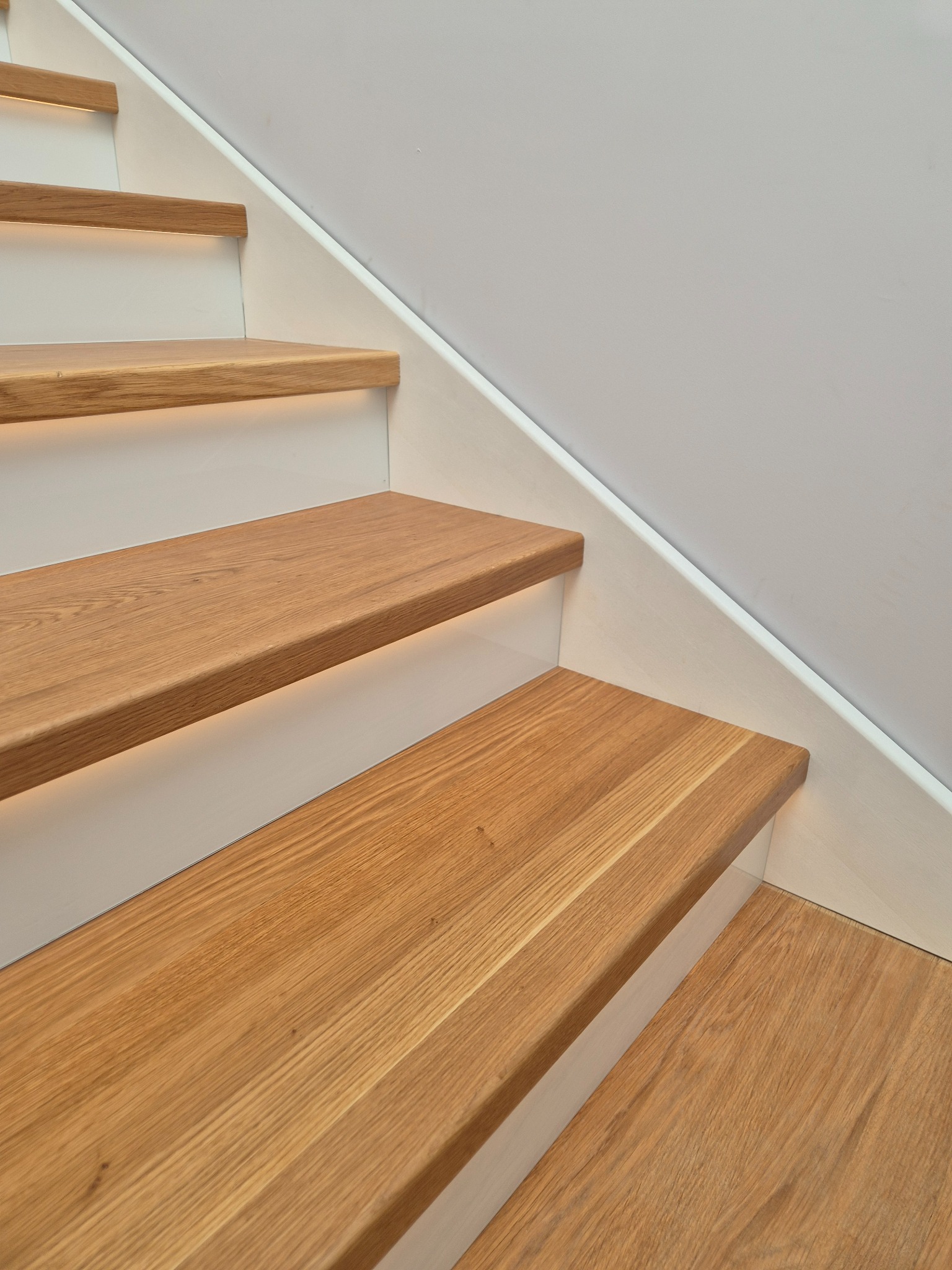 Nowoczesne schody drewniane z subtelnym podświetleniem LED, białe stopnice, jasne drewno, minimalistyczny design, widok z dołu, detale wykończenia.