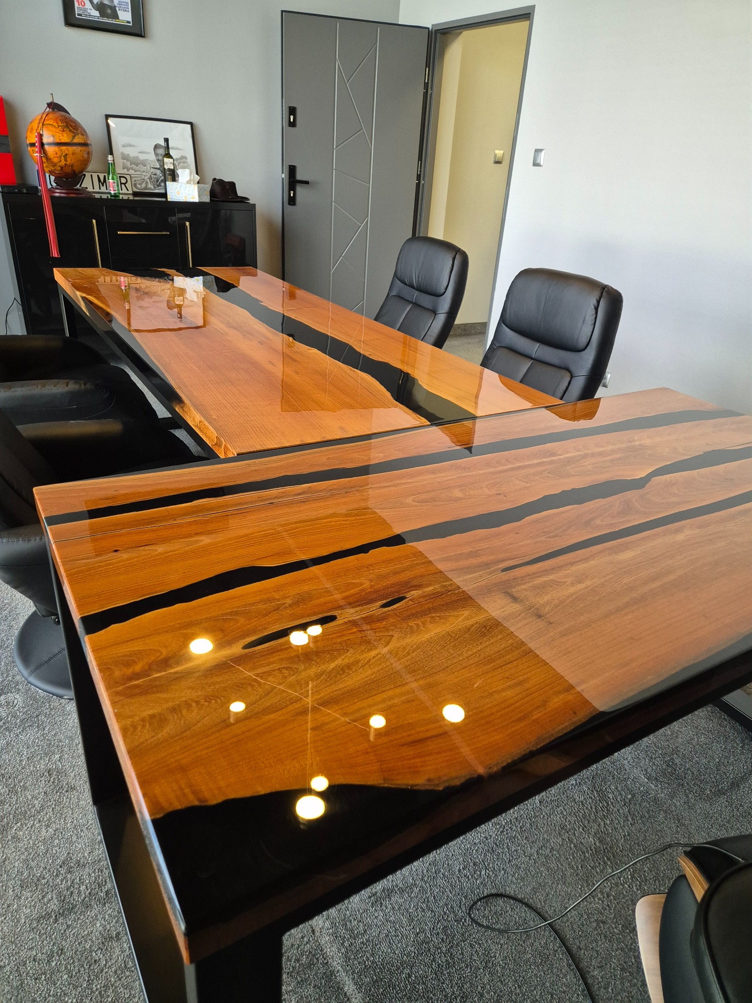 Stylowy, duży stół biurowy z drewna z czarną żywicą epoksydową, widok z góry, nowoczesne krzesła biurowe w tle, minimalistyczne wnętrze biura.