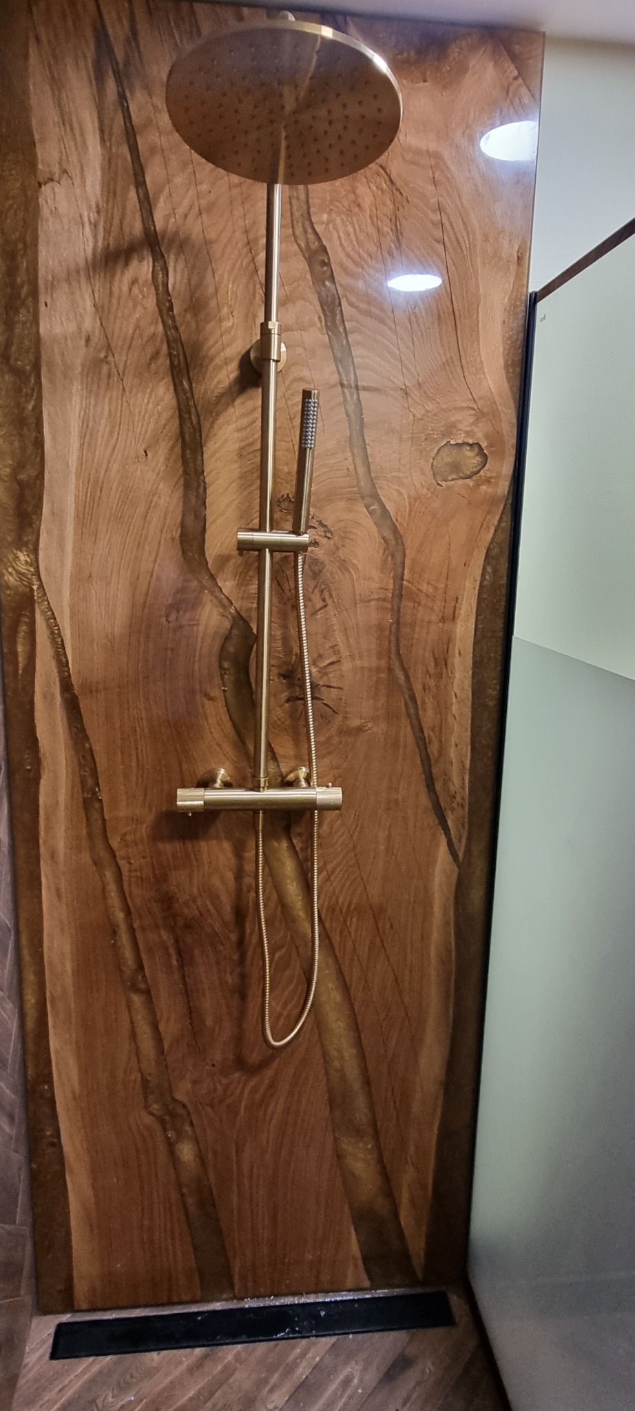 Złoty zestaw prysznicowy na tle ściany z drewna egzotycznego z żywicą epoksydową. Nowoczesny design kabiny prysznicowej z unikalnym wykończeniem.