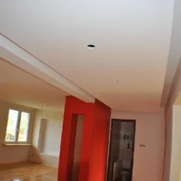 Jasne wnętrze po remoncie: parkiet, ściana akcentowa w intensywnej czerwieni, sufit z oświetleniem punktowym. Widoczny fragment łazienki.