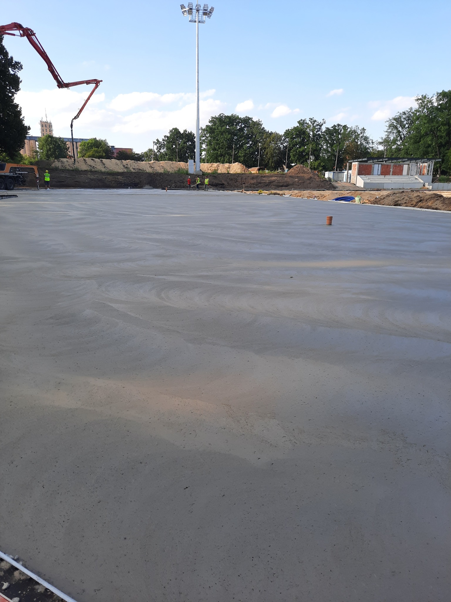 Świeżo wylana, gładka posadzka przemysłowa na budowie, z widoczną pompą do betonu w tle. Beton ma charakterystyczny wzór falisty.