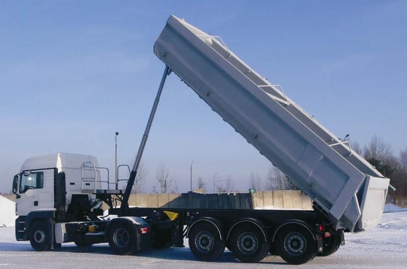 Ciężarówka wywrotka z podniesioną skrzynią ładunkową, widoczne opony, elementy hydrauliczne i błękitne niebo w tle.