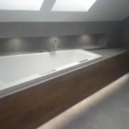 Nowoczesna łazienka na poddaszu z białą wanną obudowaną drewnopodobną okładziną i szarą płytką ceramiczną, oświetlona światłem z okien dachowych i punktowych lamp LED.