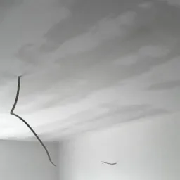 Surowy stan wnętrza: Świeżo nałożona, jeszcze wilgotna gładź na suficie, widoczne niedoskonałości i wystające przewody elektryczne, białe ściany w narożniku pokoju.