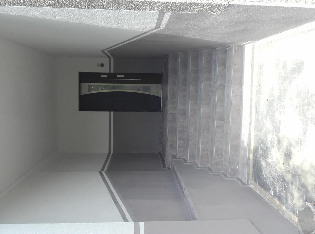 Wykończone wnętrze klatki schodowej z szarymi płytkami na schodach i ścianie, widoczna czarna szafka wnękowa z przeszkleniem, ściany pomalowane w odcieniach szarości z dekoracyjnymi paskami.