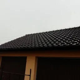 Nowo położony, ciemnobrązowy dach z dachówki ceramicznej na garażu z dwoma bramami, widok z dołu pod kątem w pochmurny dzień.