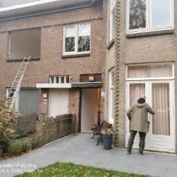 Montaż drzwi wejściowych w Opalenicy: pracownik instaluje białe drzwi z przeszkleniem w budynku z cegły, w tle widoczna drabina oparta o otwór okienny.