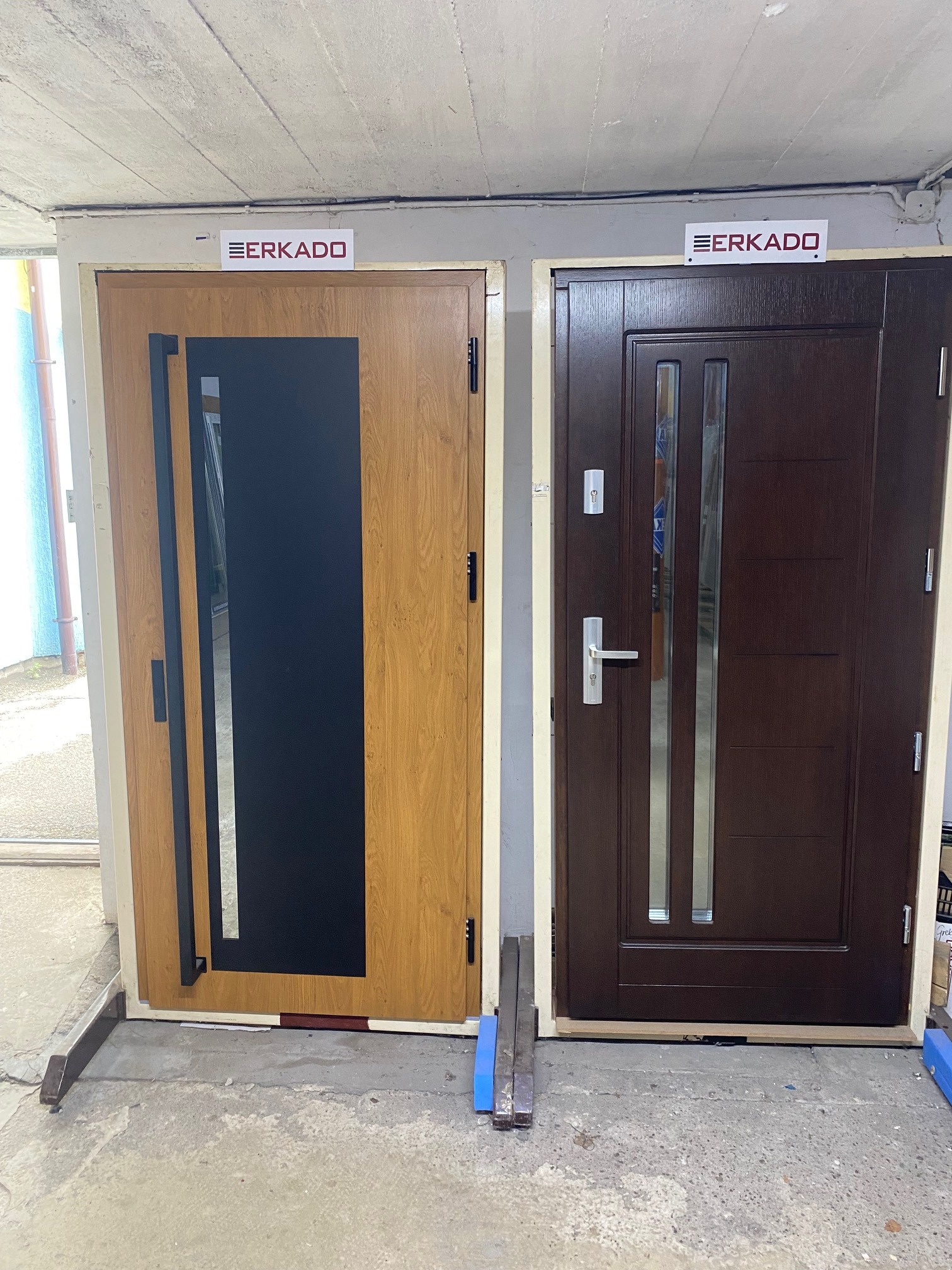 Dwa modele drzwi wejściowych marki ERKADO: po lewej model z dużym czarnym panelem i drewnianym wykończeniem, po prawej model w ciemnobrązowej okleinie z podłużnymi przeszkleniami.