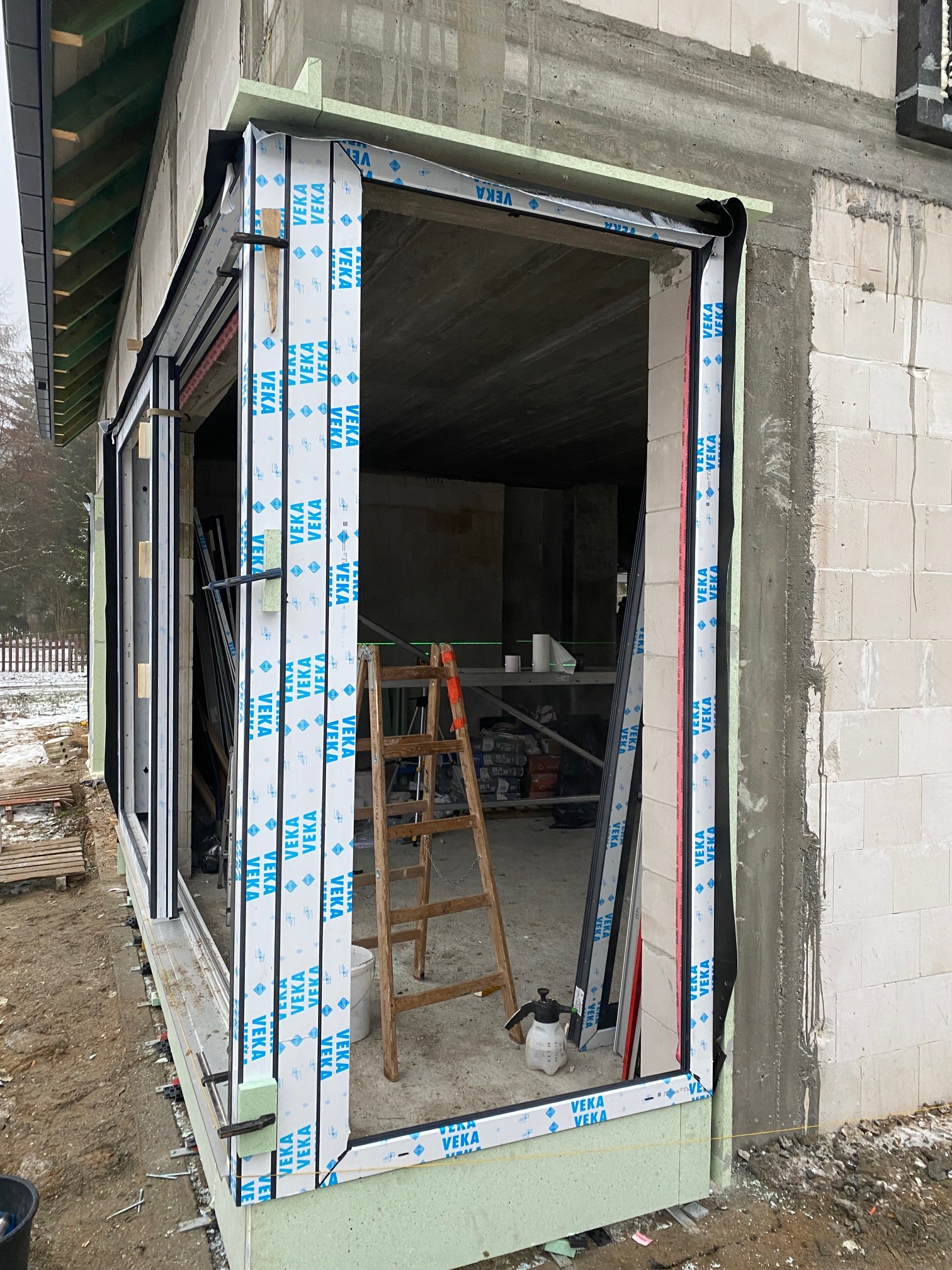 Montaż okna z profili VEKA w surowym stanie budynku, widoczna drabina, narzędzia i materiały budowlane wewnątrz.