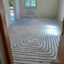 INSTAL-SANIT Adam Zaręba - Frezowane rowki w podkładzie podłogowym, przygotowane pod montaż rur ogrzewania podłogowego, układane spiralnie w przestronnym, jasnym pomieszczeniu z oknem.