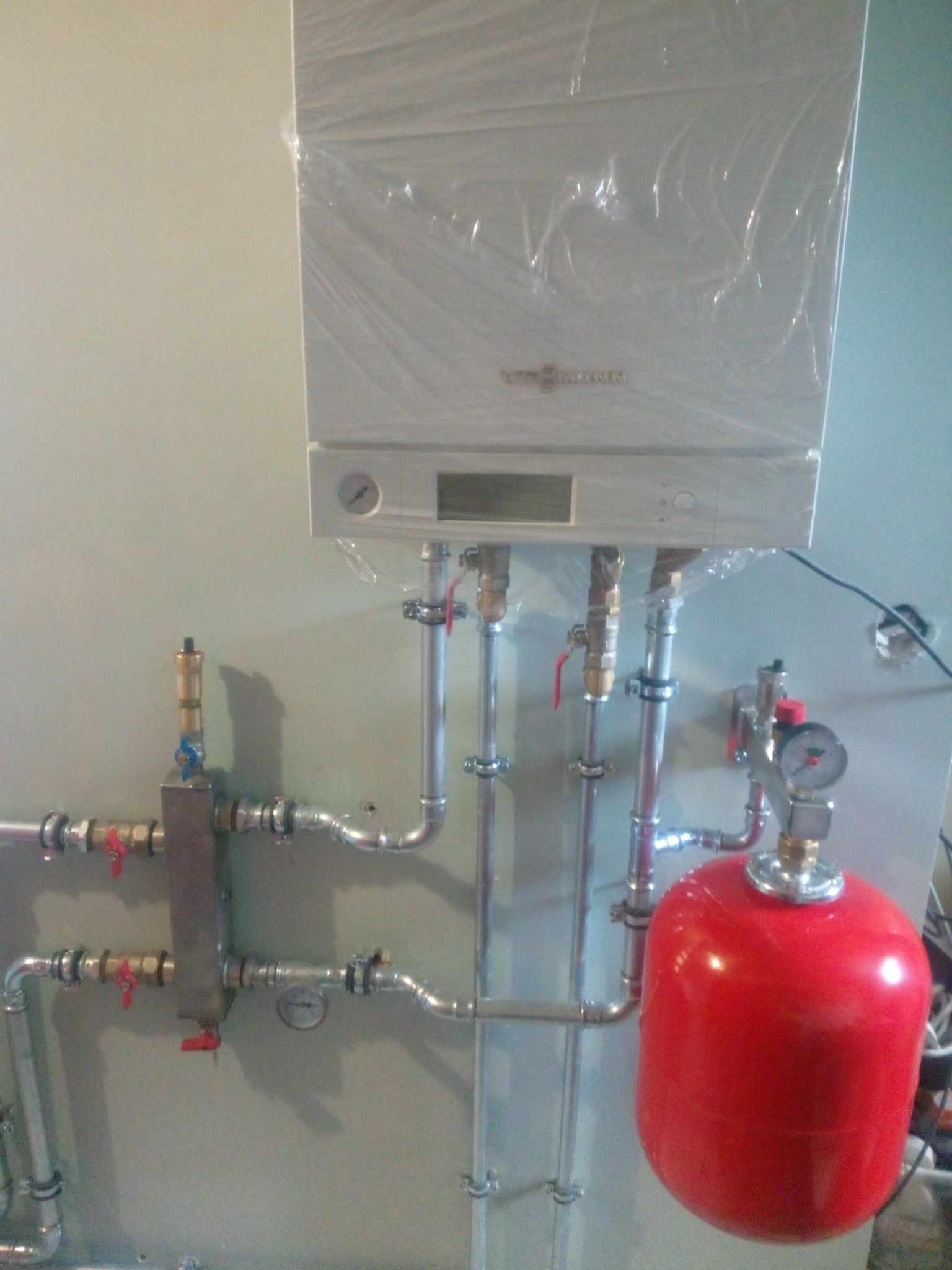 Nowy piec gazowy Viessmann, jeszcze w folii ochronnej, podłączony do instalacji z czerwonym zbiornikiem wyrównawczym i licznymi zaworami kulowymi.