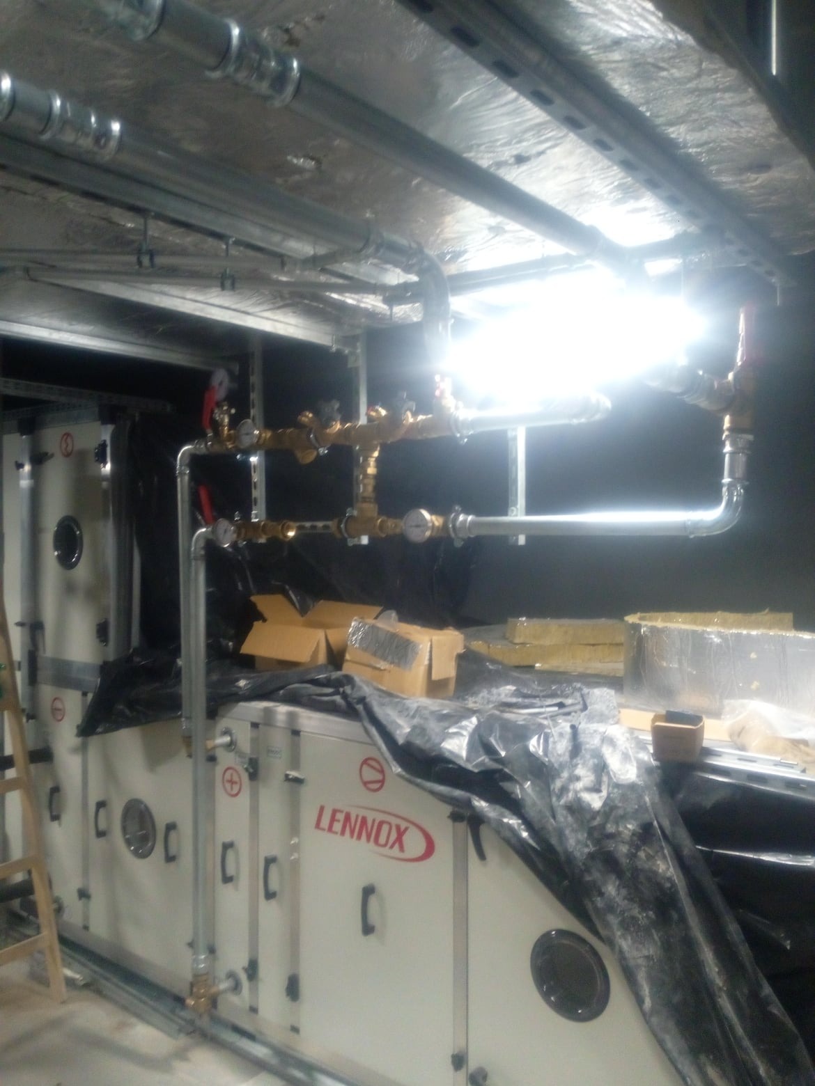Instalacja rur i zaworów nad centralą wentylacyjną Lennox, widoczne manometry i izolacja termiczna, instalacja w trakcie montażu.