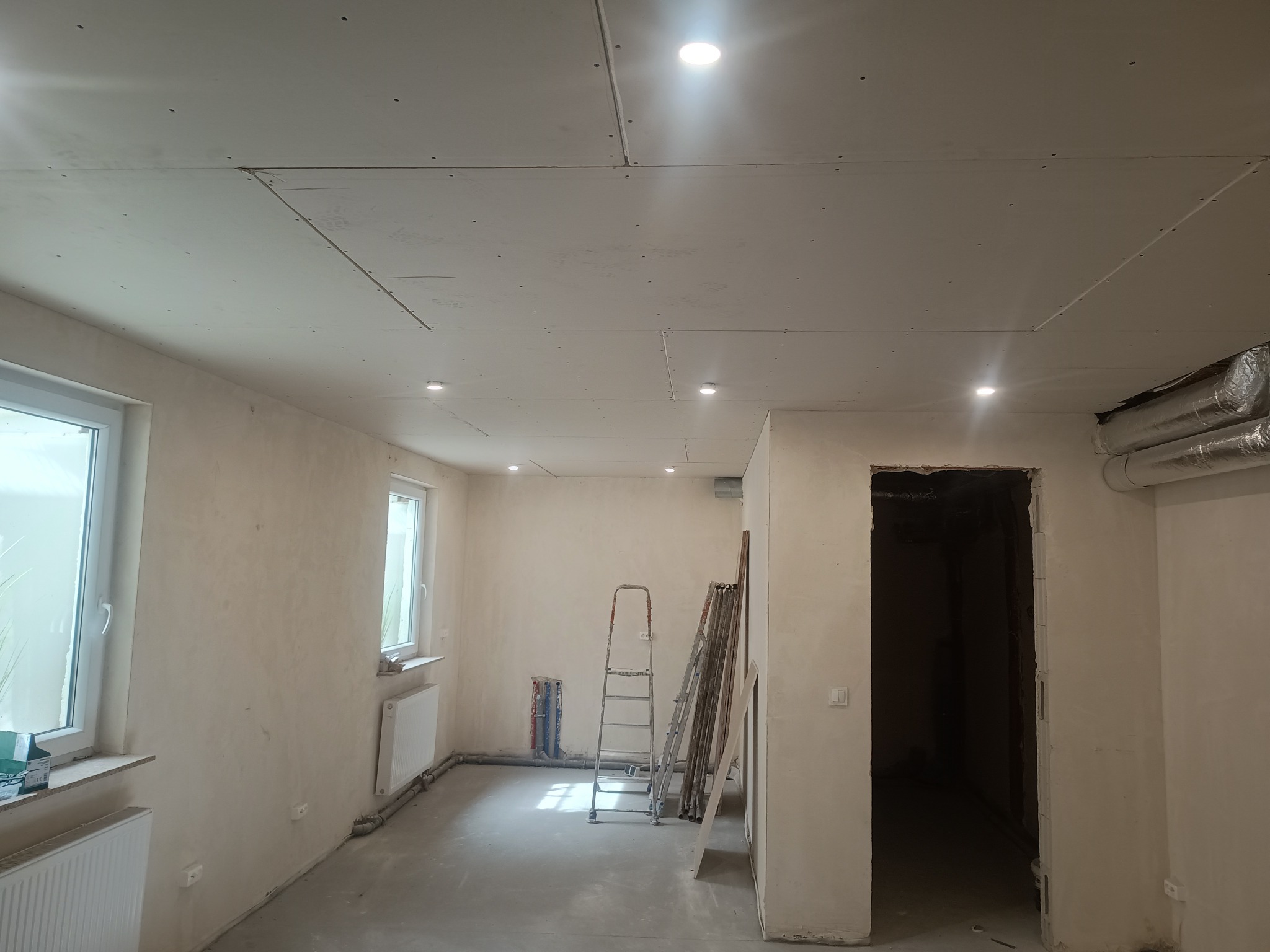 Wnętrze w trakcie remontu: sufit z płyt kartonowo-gipsowych z zamontowanymi punktowymi lampami, ściany przygotowane do malowania, drabina w pomieszczeniu.