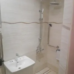 Wyremontowana łazienka z beżowymi płytkami, umywalką z szafką, kabiną prysznicową z deszczownicą i uchwytem dla niepełnosprawnych.