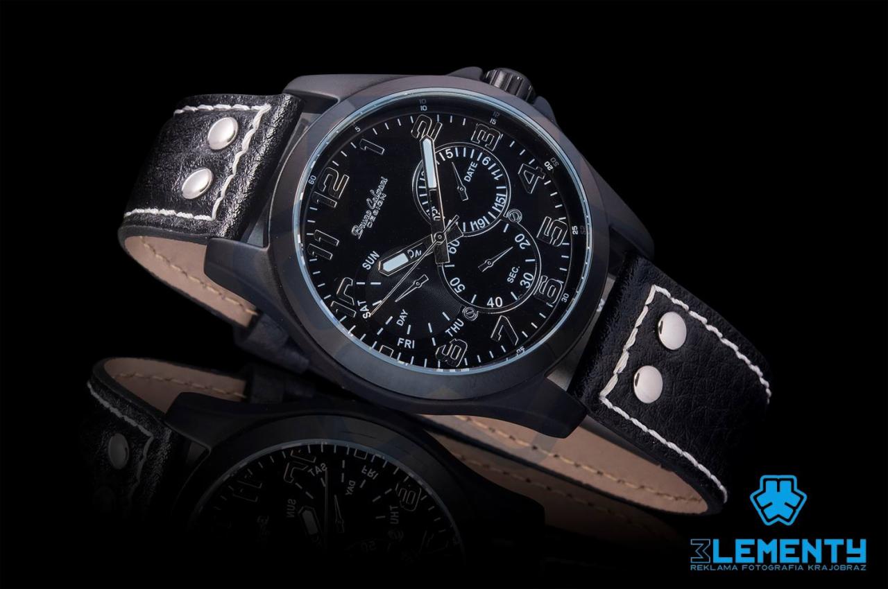 Czarny męski zegarek z dużym cyferblatem i skórzanym paskiem z metalowymi nitami, leżący na czarnej, odbijającej powierzchni. Widoczne logo fotografa.
