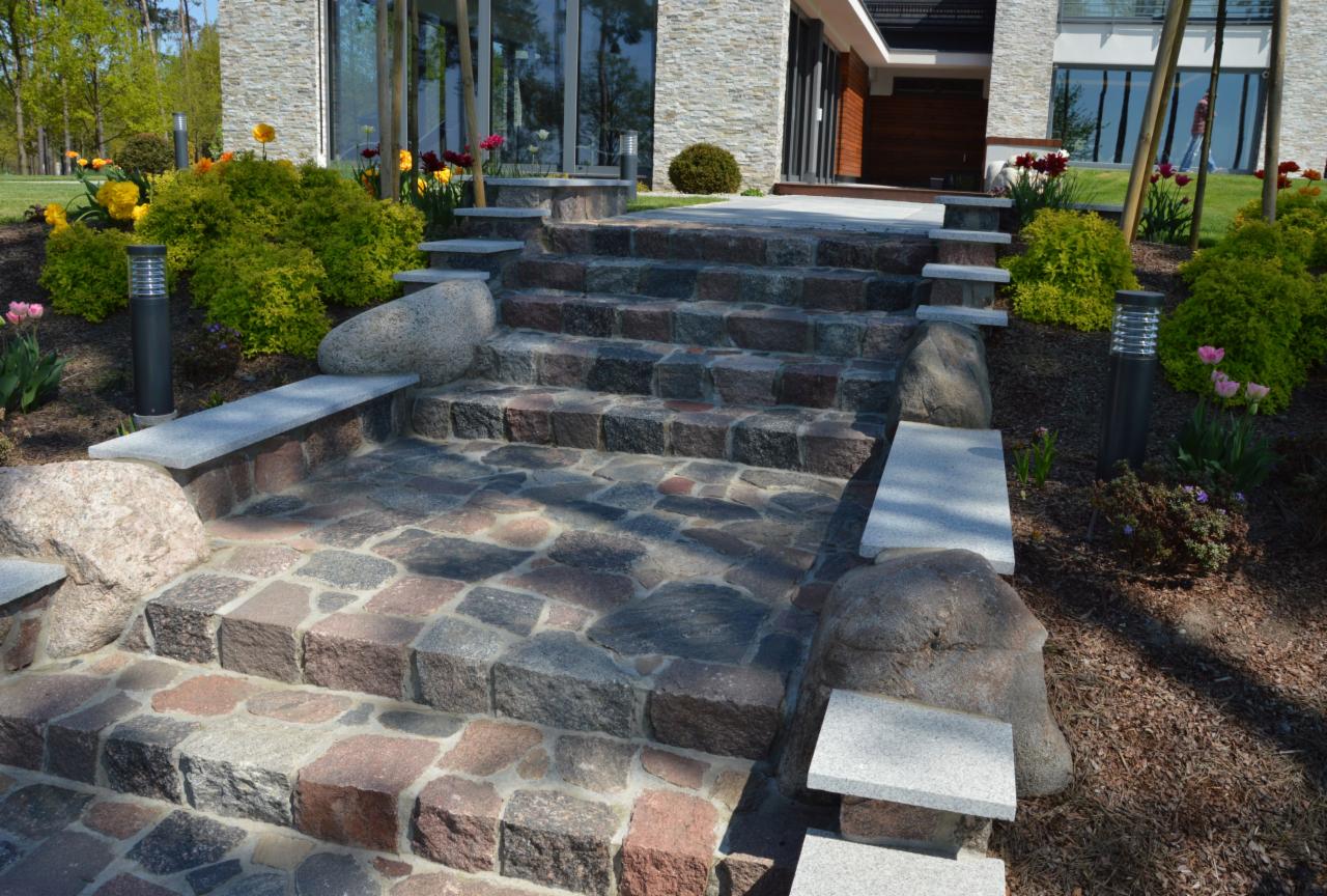 Kamienne schody prowadzące do domu, z elementami dekoracyjnymi z jasnego kamienia i otoczone roślinnością.