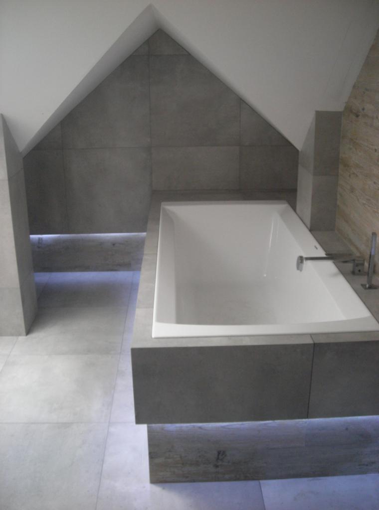 Minimalistyczna łazienka na poddaszu z wanną obudowaną szarą płytką i subtelnym oświetleniem LED pod wanną i wzdłuż ściany.