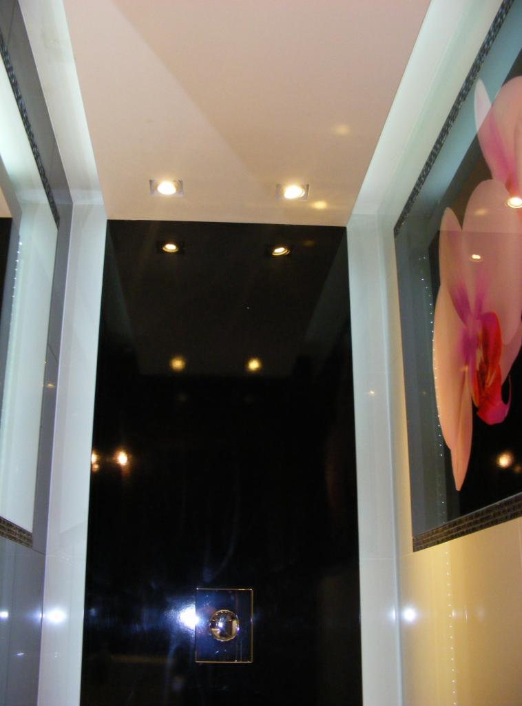 Nowoczesna łazienka z czarnymi, błyszczącymi panelami ściennymi, punktowym oświetleniem sufitowym i dekoracyjnym panelem z motywem orchidei.