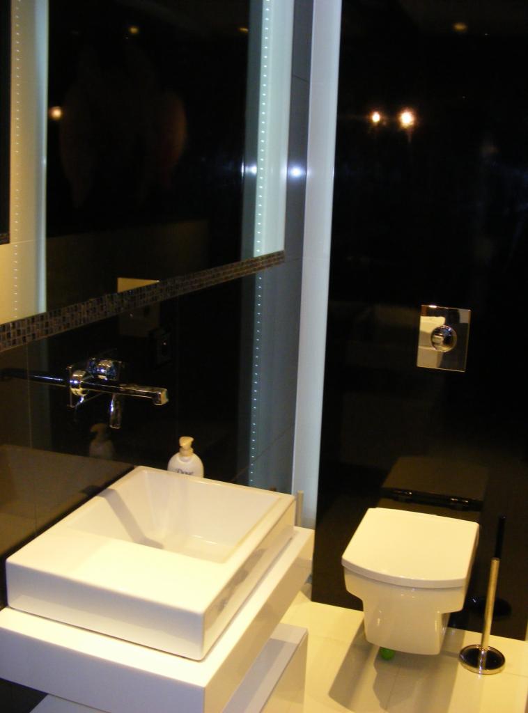 Minimalistyczna łazienka z czarnymi ścianami, białą umywalką na postumencie i toaletą. Oświetlenie punktowe i dekoracyjne listwy LED.