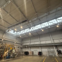 RS-MAL - Wnętrze hali produkcyjnej z widoczną konstrukcją dachu, oświetleniem i instalacjami, ściany pomalowane na jasny kolor.