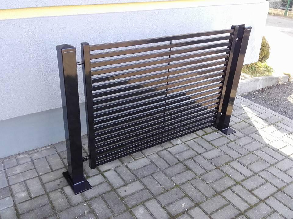 Nowoczesna, czarna, metalowa brama posesyjna z poziomymi szczeblami, zamontowana na kostce brukowej. Minimalistyczny design, widoczne detale mocowania.