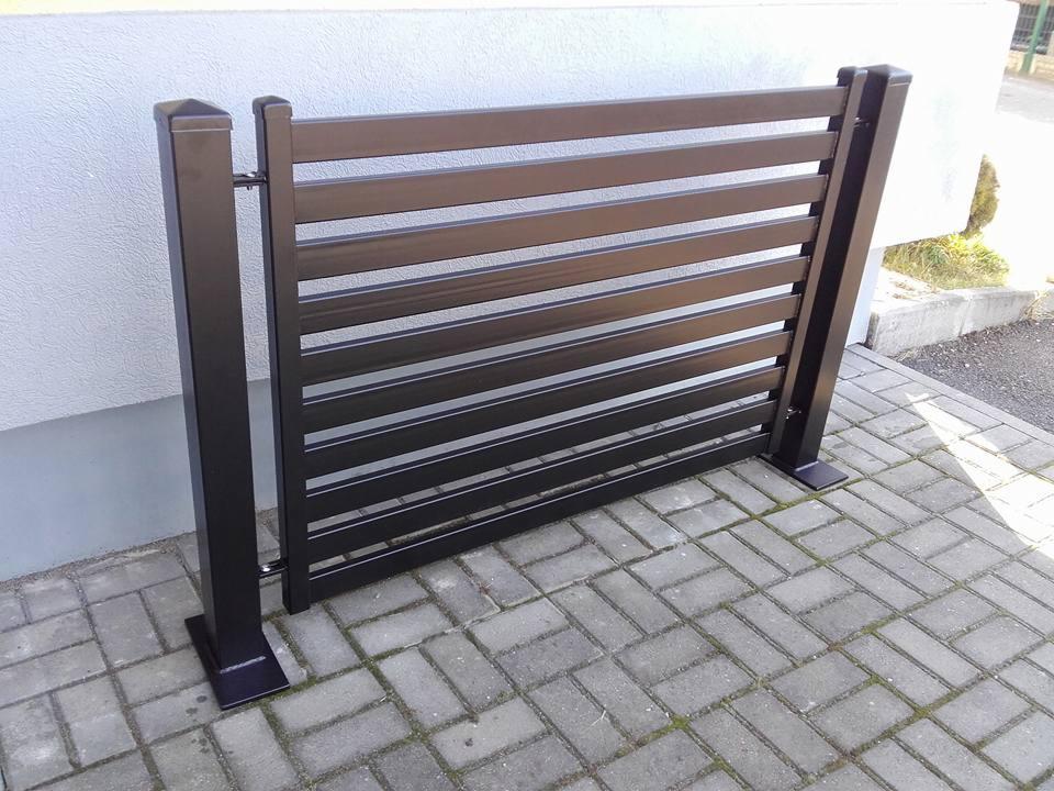 Nowoczesna, pozioma brama w kolorze antracytu z metalowych profili, zamontowana na kostce brukowej. Widoczne detale mocowania i minimalistyczny design.