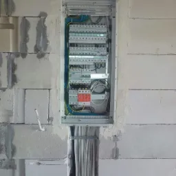 Rozdzielnica elektryczna z widocznymi przewodami w ścianie z betonu komórkowego, w trakcie montażu.