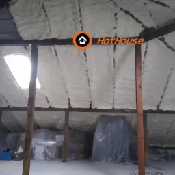 Poddasze po ociepleniu pianką poliuretanową, widoczne drewniane elementy konstrukcyjne dachu, okno dachowe, zabezpieczone folią przedmioty.