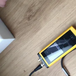 Pomiar wilgotności ściany za pomocą elektronicznego wilgotnościomierza Trotec T3000 z sondą kulkową na drewnianej podłodze.