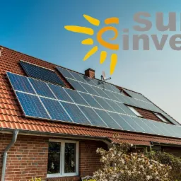 Czerwony, dwuspadowy dach z panelami słonecznymi i kolektorami słonecznymi, widoczny z poziomu gruntu, z logo firmy Sun Invest na niebie.