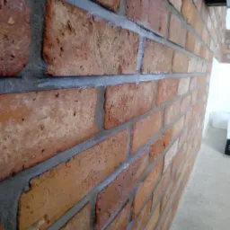 Ściana z czerwonej cegły klinkierowej z szarą fugą, ułożona pod kątem z widoczną perspektywą i fragmentem sufitu.