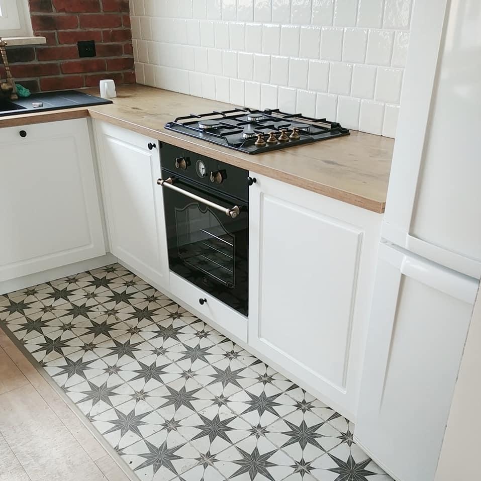Wykończona kuchnia z białymi szafkami, drewnianym blatem, czarną płytą gazową i piekarnikiem oraz wzorzystą podłogą w gwiazdy.