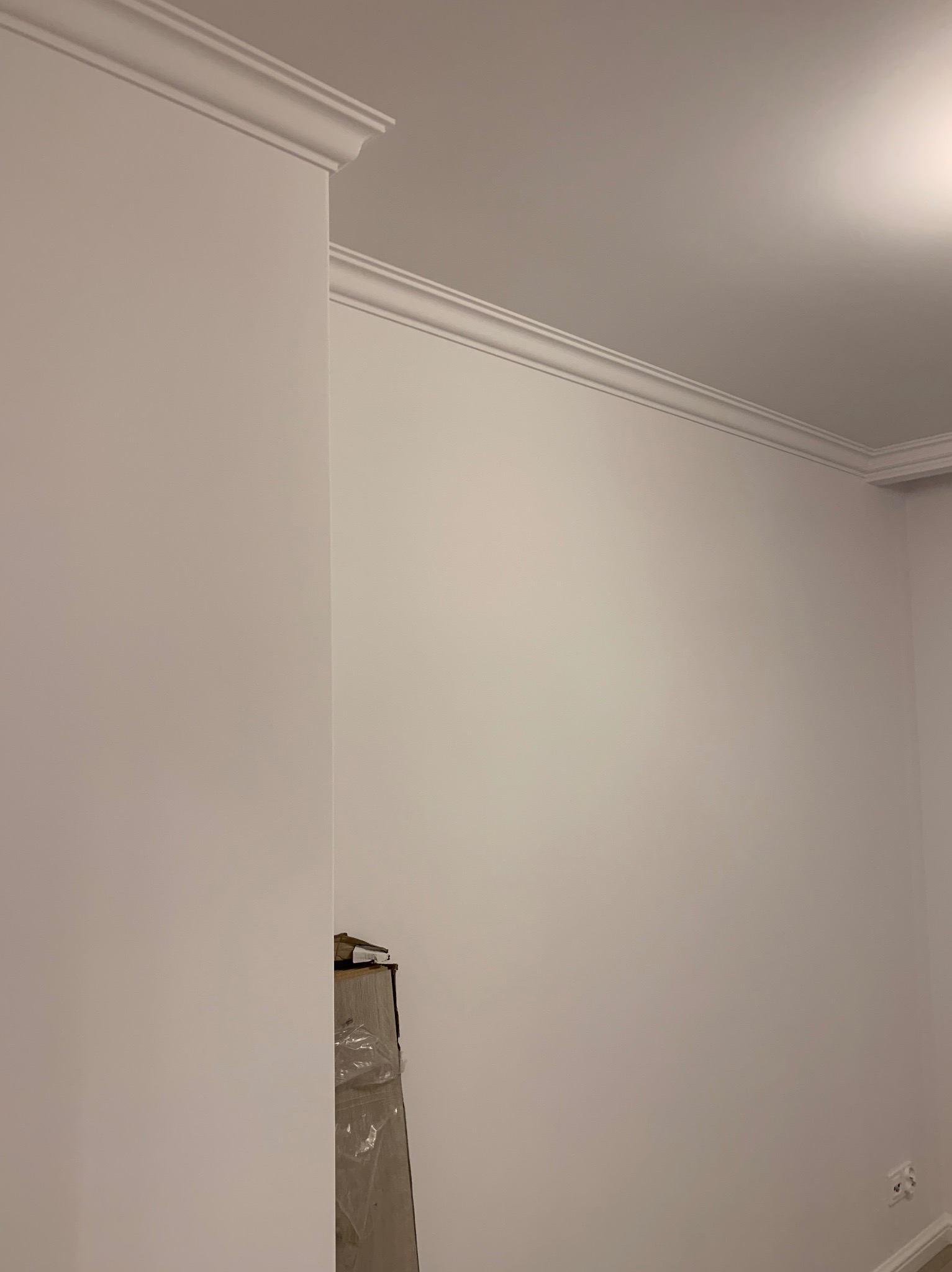 Świeżo pomalowane, jasne ściany z dekoracyjnymi listwami przysufitowymi, widoczne materiały budowlane w rogu pomieszczenia.