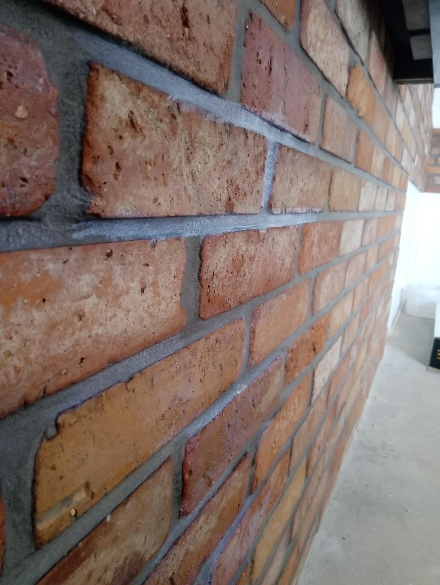 Ściana z czerwonej cegły klinkierowej z szarą fugą, ułożona pod kątem z widoczną perspektywą i fragmentem sufitu.