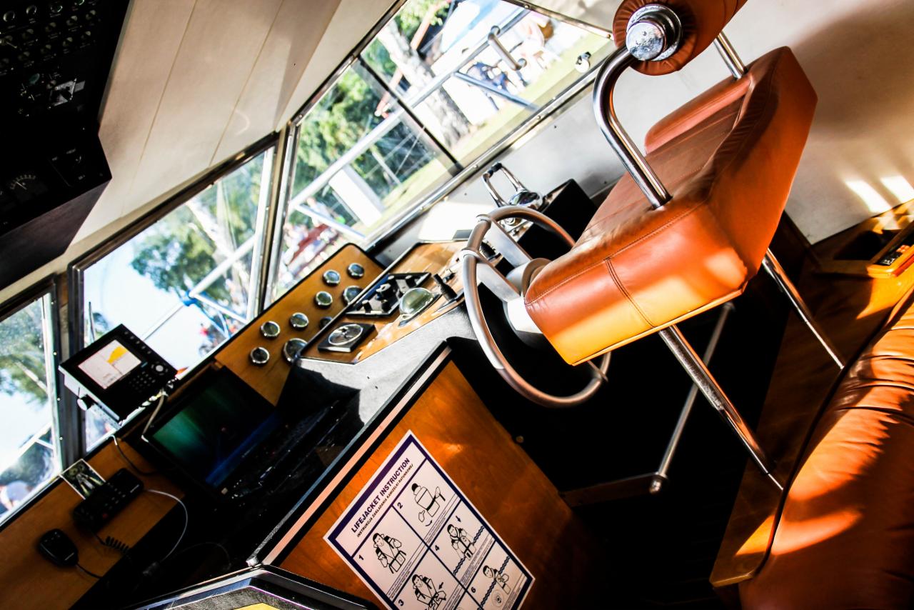 Wnętrze kabiny sterowniczej łodzi z brązowym skórzanym fotelem, panelem sterowania z licznymi przełącznikami i instrukcją obsługi kamizelki ratunkowej.