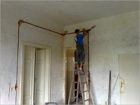 Instalacja odgromowa w starym domu: monter na drabinie mocuje miedziany przewód odprowadzający wzdłuż ściany, widoczne złącza i surowy tynk.