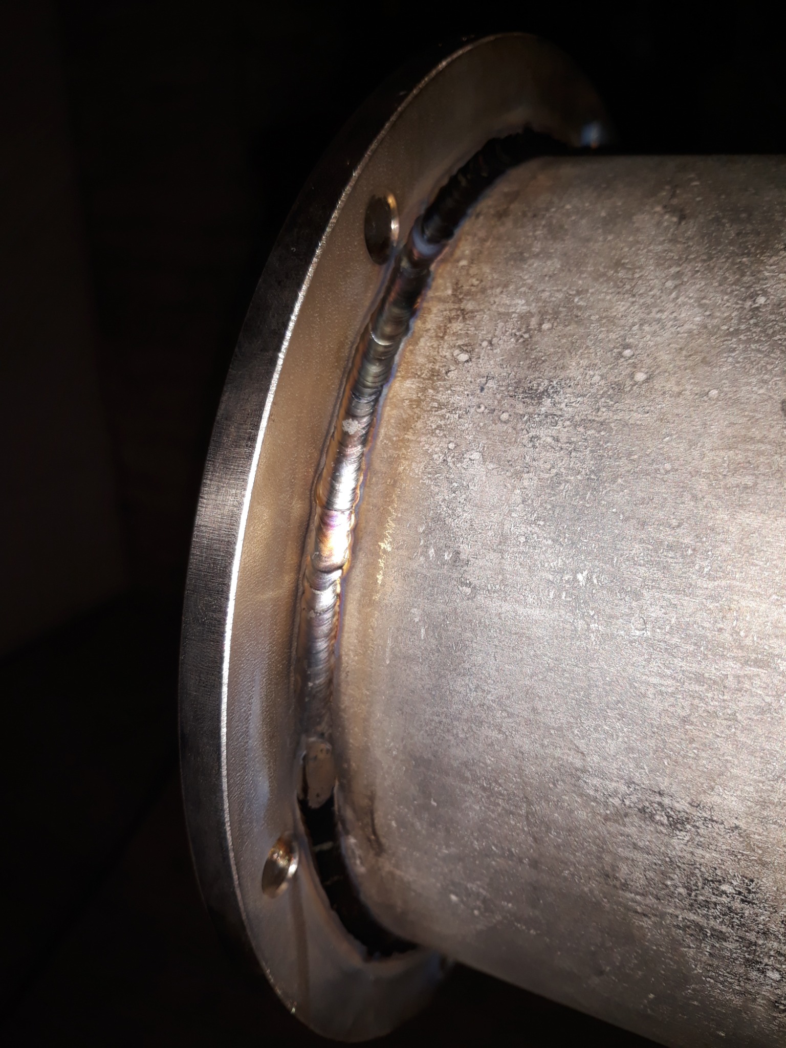 Szczegółowe zbliżenie spoiny łączącej rurę ze stalowym kołnierzem, widoczne ślady obróbki i przebarwienia termiczne.