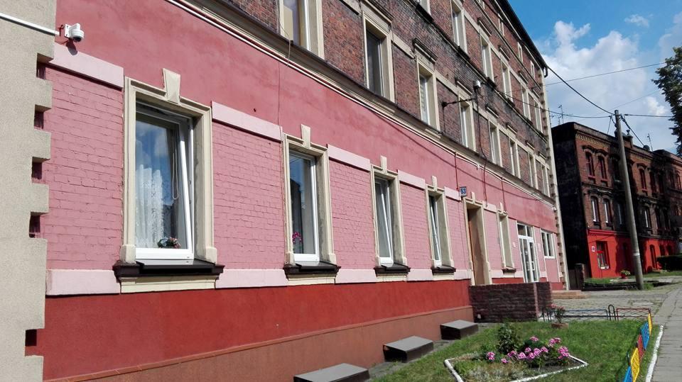 Kamera monitoringu zamontowana na rogu budynku mieszkalnego z cegły pomalowanego na różowo, widok z zewnątrz na kilka okien z białymi ramami.