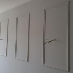 Projekt RS - Ściana z trzema dekoracyjnymi panelami z listwami, z wystającymi przewodami elektrycznymi z dwóch paneli i oknem z boku.