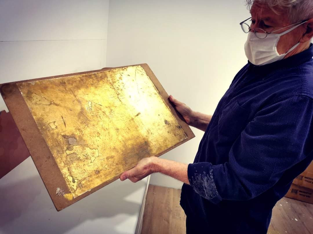 Pracownik w maseczce trzyma w rękach płytę z nałożonym złotym, nieregularnym wzorem, prawdopodobnie do dekoracji ścian.