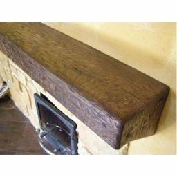 Drewkomplet Spółka z Ograniczoną Odpowiedzialnością - Rustykalna, ciemnobrązowa belka drewniana nad kominkiem z kamienia, z widoczną fakturą drewna i metalowymi elementami kominka. Ciepłe oświetlenie.