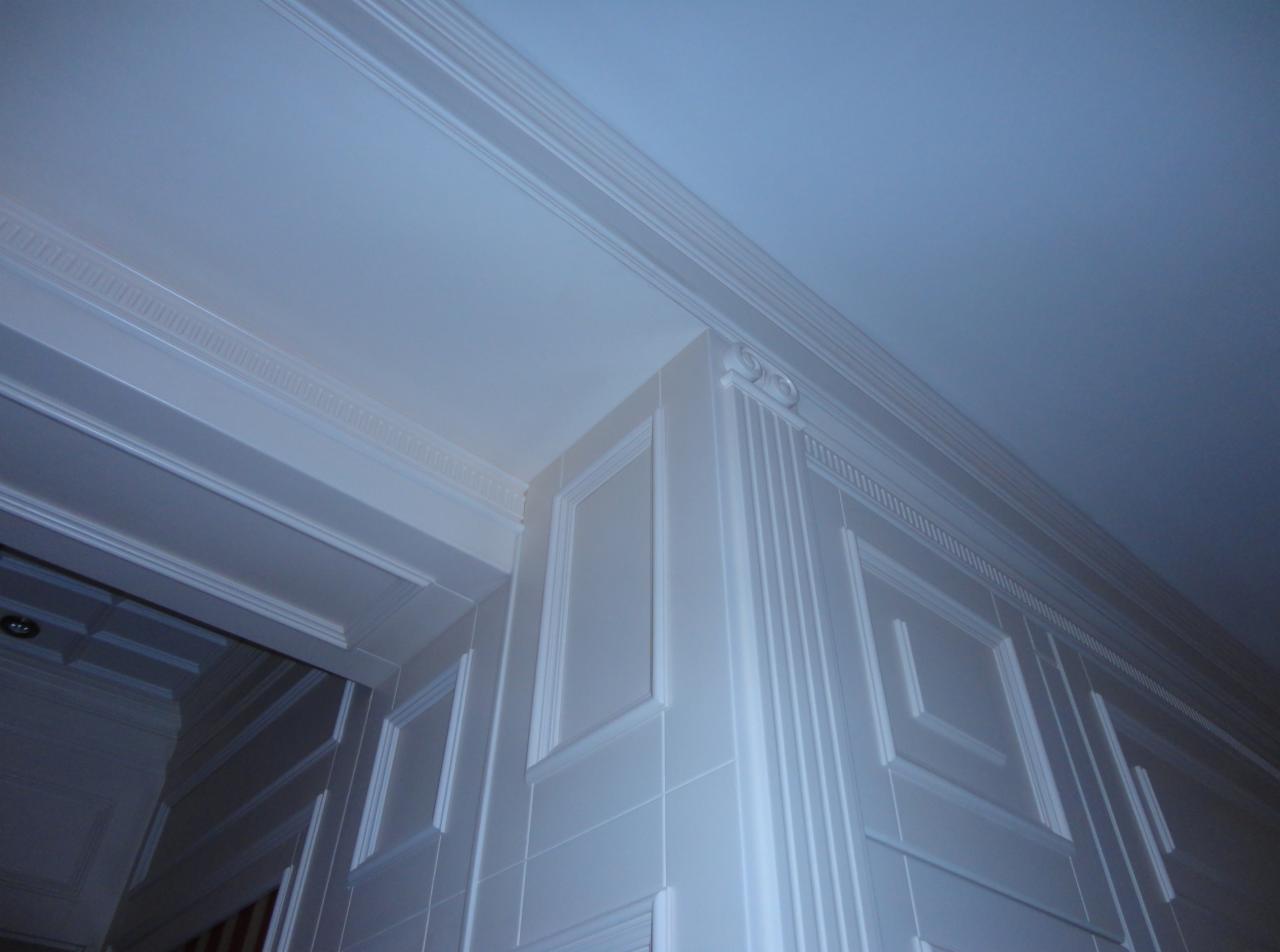 Detal wykończenia wnętrza: białe, kasetonowe ściany i sufit z dekoracyjnymi listwami. Ujęcie z dołu, widoczny fragment ościeżnicy drzwiowej.