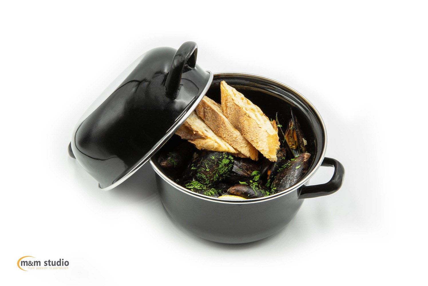 Czarny garnek z otwartą pokrywką, wypełniony małżami, ziołami i kromkami chleba na białym tle. Profesjonalne oświetlenie podkreśla detale potrawy.