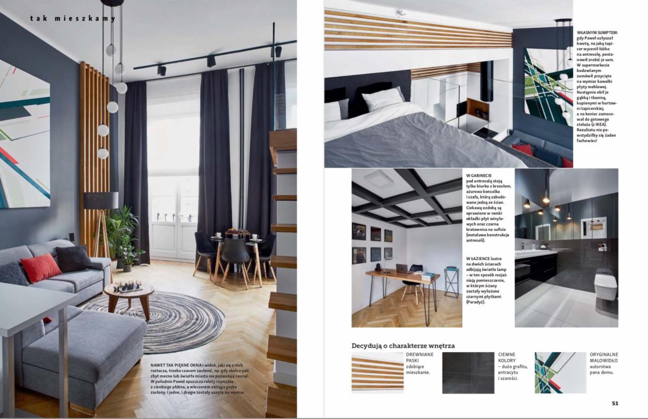 Salon z szarą sofą, okrągłym dywanem i drewnianą ścianką działową, oświetlony wiszącymi lampami kulami, widok na stół z krzesłami i okno z ciemnymi zasłonami.