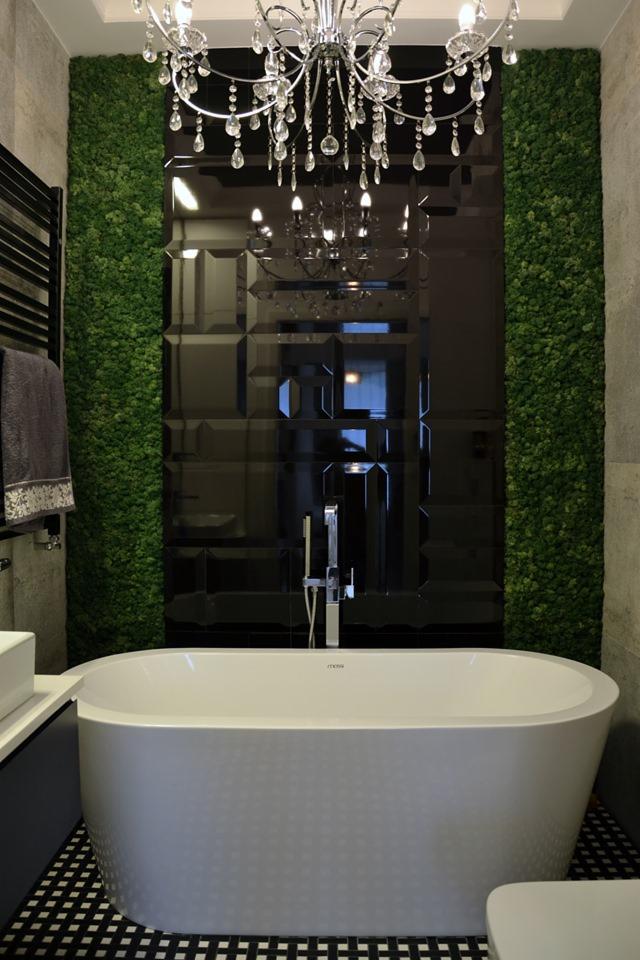 Nowoczesna łazienka z wolnostojącą wanną, czarnymi lustrzanymi płytkami, ścianą z mchu i kryształowym żyrandolem.